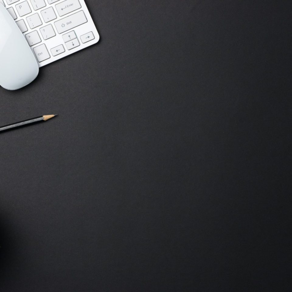 A black desk with a keyboard, a mouse, a pencil, and a small plant.